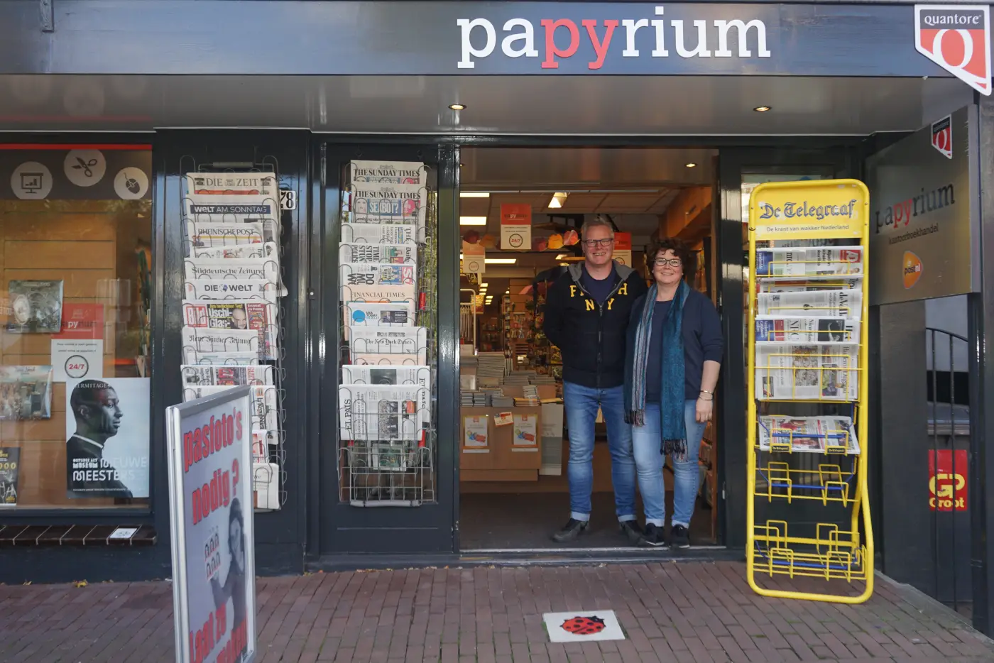 Peter en Yvonne Slofstra staan lachend in de deuropening van Papyrium, met kranten in de rekken naast de deur